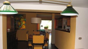 Una mesa de billar con bolas, una zona de comedor con sillas y dos lámparas colgantes.