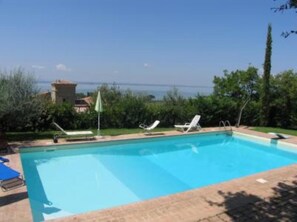 A rectangular swimming pool with clear blue water, surrounded by a paved deck. There are two lounge chairs and a small umbrella on the deck. - Villa with swimming pool and garden- San Feliciano, Trasimeno lake (San Feliciano)