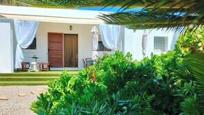 Un bâtiment blanc doté d’un patio couvert, d’une porte et d’une fenêtre. Des plantes se trouvent devant le bâtiment.