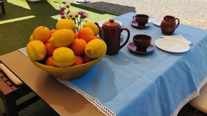 Une table dressée à l’extérieur, avec un saladier de fruits, un service à café et une vue sur un jardin aménagé.