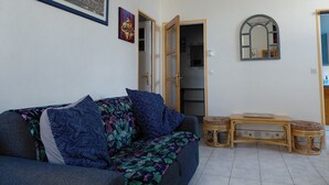 Una sala de estar con un sofá, una mesita, un espejo y una puerta que da a otra habitación.