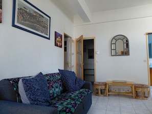 Un salon comprenant un canapé, une petite table, un miroir et une porte donnant sur une autre pièce.