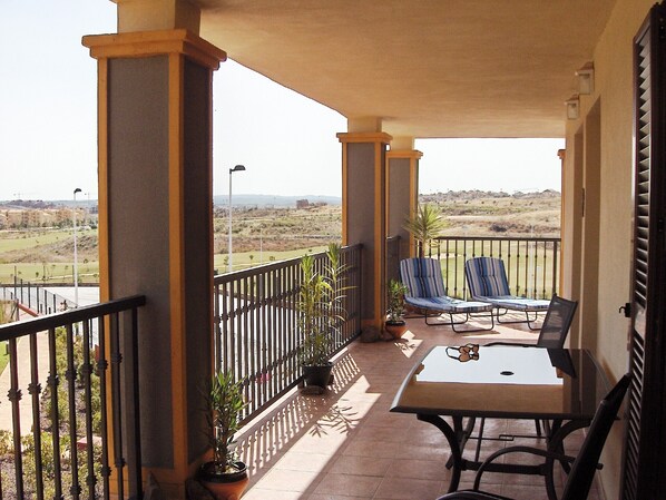 A balcony with two chairs and a table, potted plants, and a view of a distant landscape.