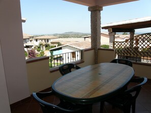 A balcony with a round table and chairs, a view of the surrounding buildings, and a clear sky.