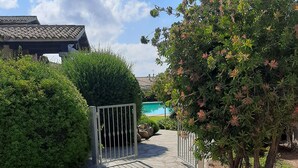 A stone pathway leading to a gated pool area with a clear view of the pool and surrounding greenery. - Nice apartment with roof terrace in an elegant complex with swimming pool (San Teodoro)