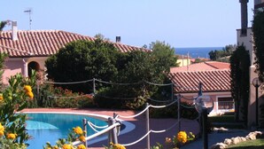 A pool area with a clear view of the sea, surrounded by buildings with red-tiled roofs and a fenced garden area. - Nice apartment with roof terrace in an elegant complex with swimming pool (San Teodoro)