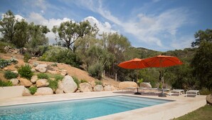 A swimming pool with a red umbrella, surrounded by rocks and trees. - Villa sea view heated pool 8 persons with electric charging point (Sainte Lucie de Porto Vecchio)