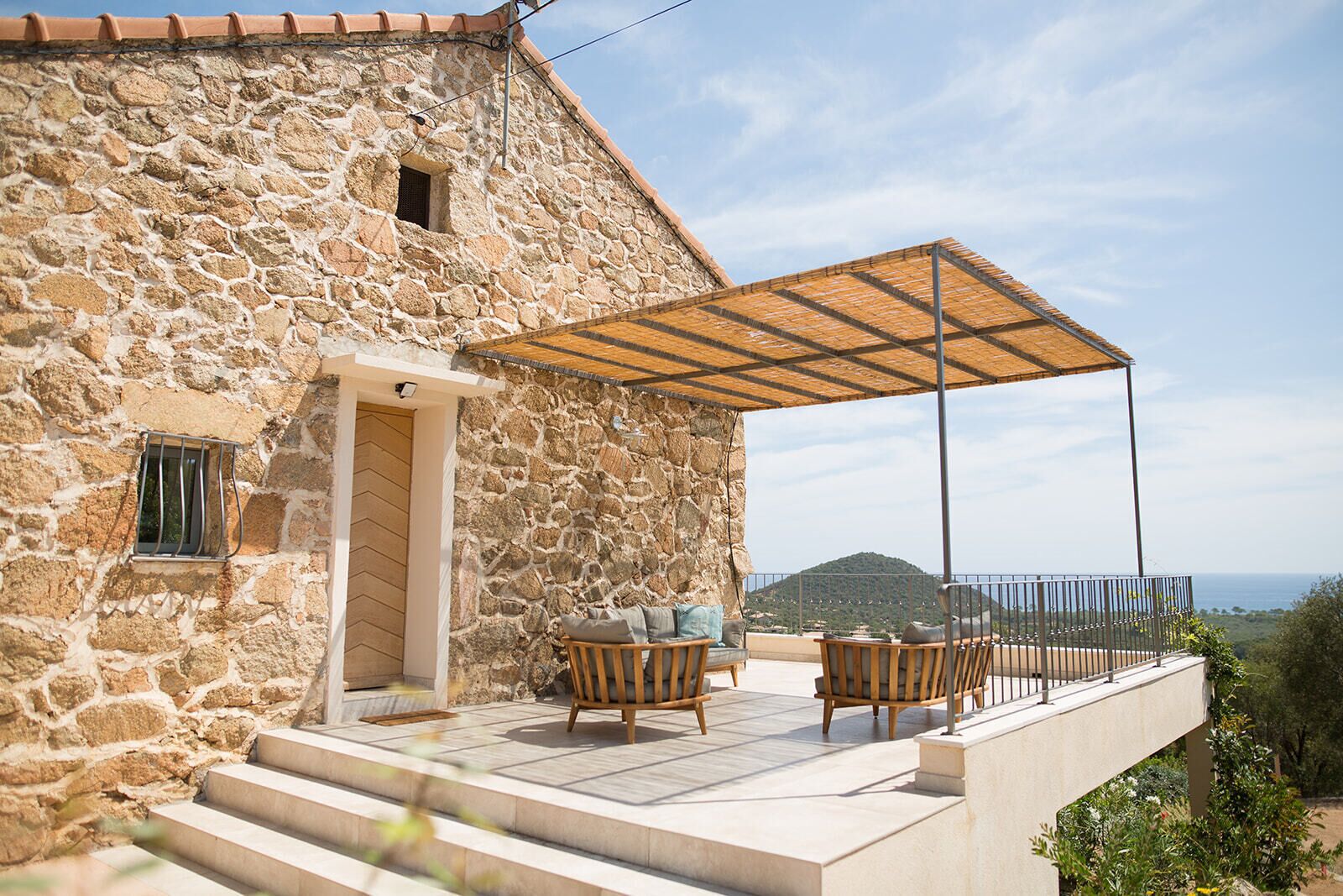 A stone building with a covered patio, outdoor seating, and a view of the sea.
