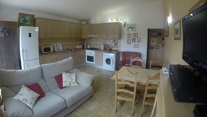 A compact living space with a kitchenette, a sofa with cushions, a dining table with chairs, and a flat-screen TV.