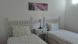 A bedroom with two single beds, a nightstand with a lamp, and a wall-mounted picture.