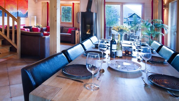 Un comedor con una larga mesa de madera dispuesta para una comida, una chimenea y vistas al exterior.