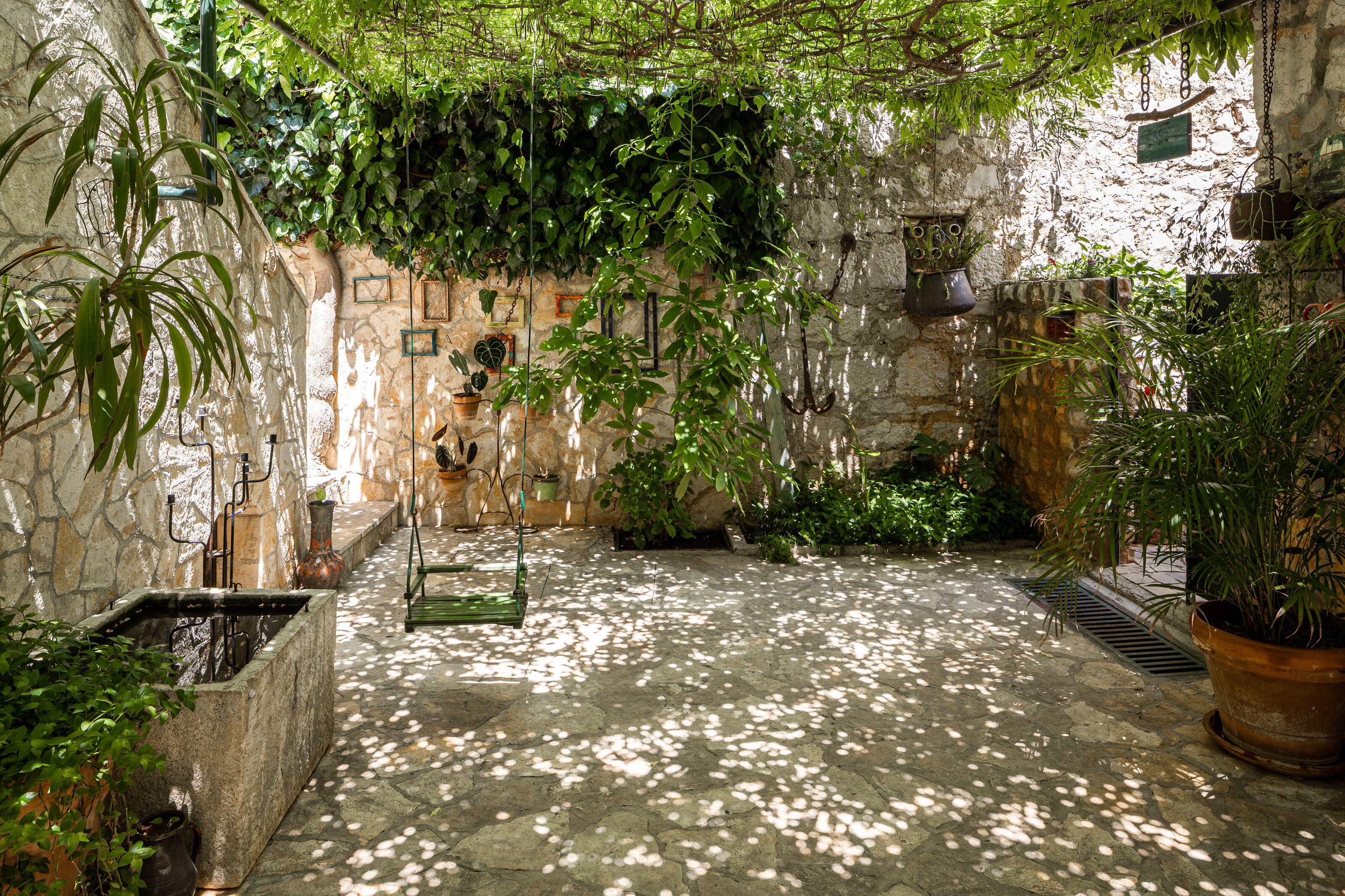 A stone courtyard with potted plants, a hanging chair, and a stone wall with a rustic appearance.