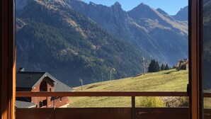 A mountain view from a wooden balcony with a house in the foreground. - Apartment Harikoa, sleeps 5, next to piste, Col de Merdassier. (Manigod)