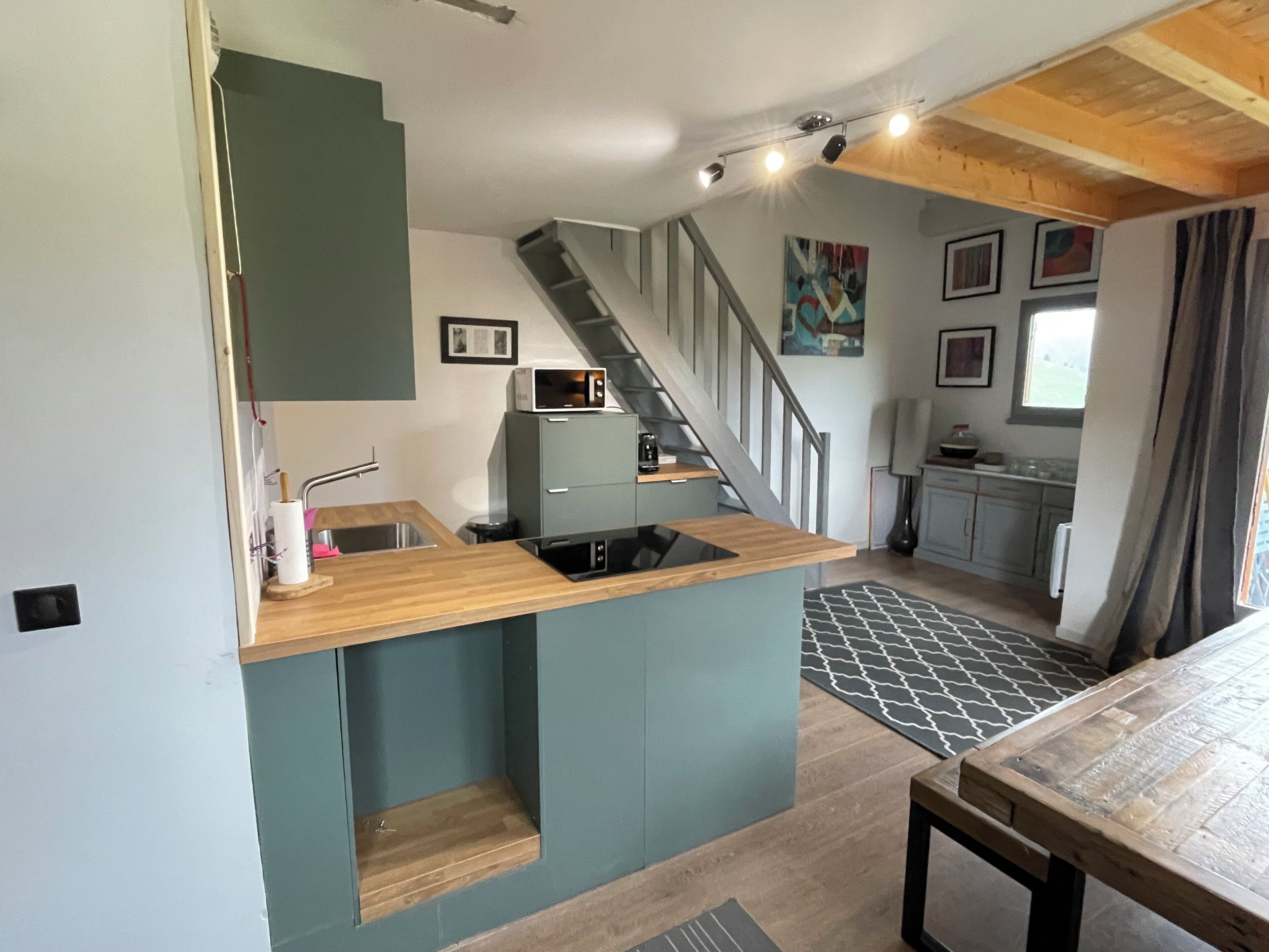 A compact kitchen with a wooden countertop, a built-in microwave, and a sink. There is a staircase leading to another level.