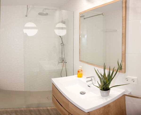 A modern bathroom with a glass shower enclosure, a white sink with a wooden vanity, and a large mirror. - LUXURIOUS PENTHOUSE ON THE BEACH (MODERN DESIGN) (Alcúdia)