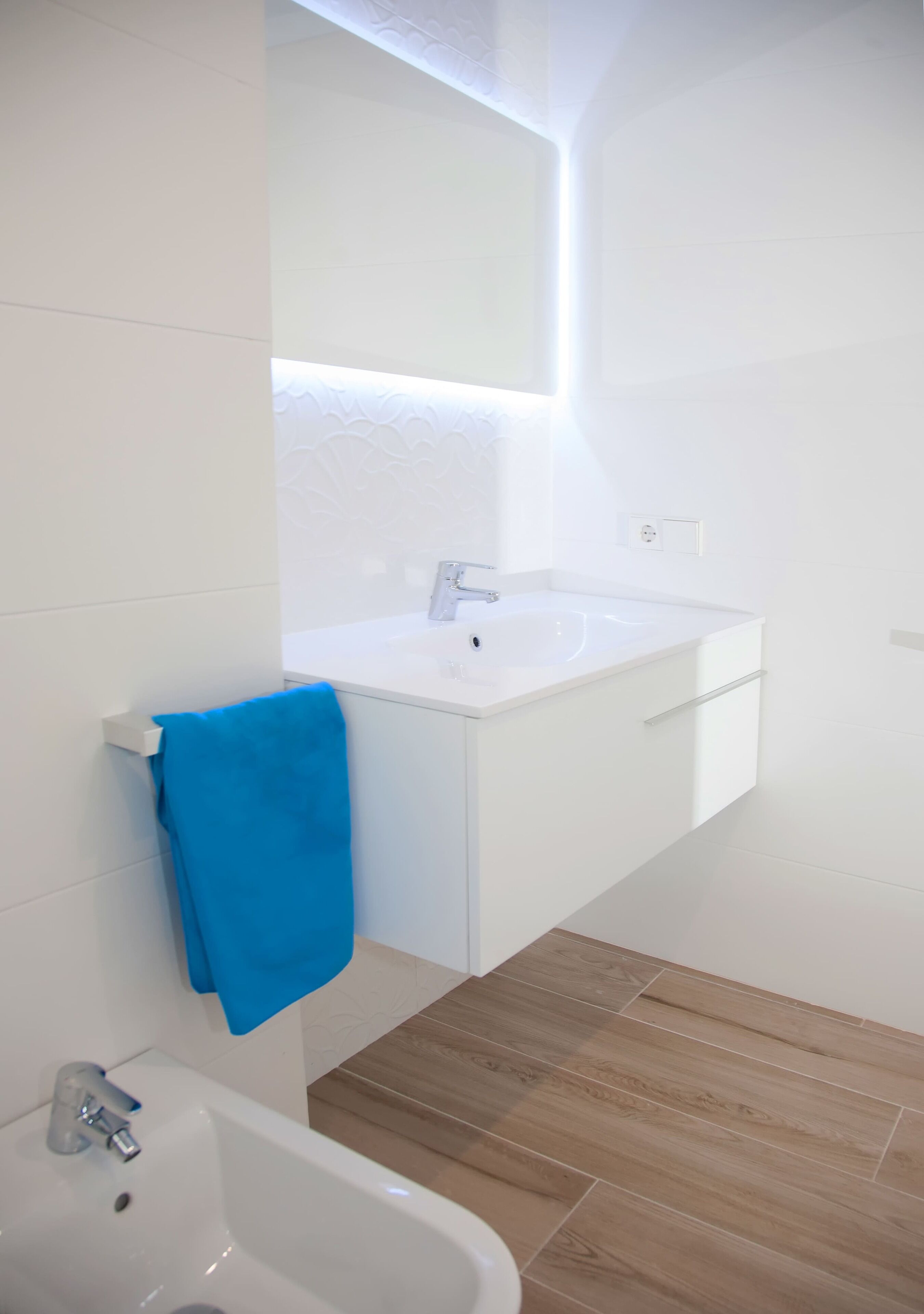 A modern bathroom with a white sink, a blue towel, and a wooden floor.