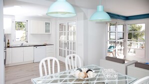 Une cuisine moderne avec des meubles blancs, une table à manger en verre et une vue sur l’extérieur.