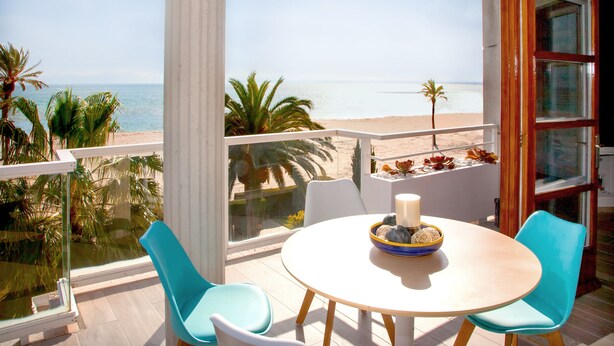 Un balcon donnant sur la plage, une table ronde avec des chaises et une bougie sur la table.