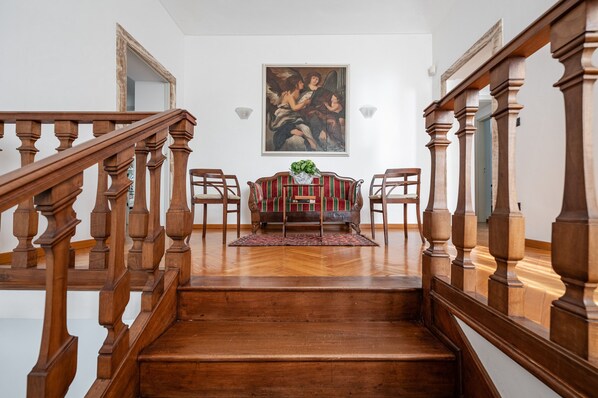 A wooden staircase with a mirror on the wall, a red and green sofa, and a painting above the sofa.