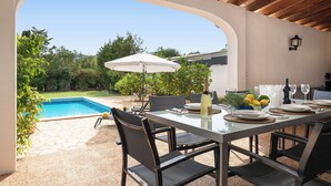 An outdoor dining area with a pool view, stone flooring, and a wooden ceiling.