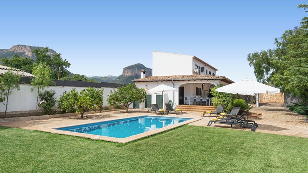 A backyard with a swimming pool, a patio with outdoor furniture, and a view of a mountain.