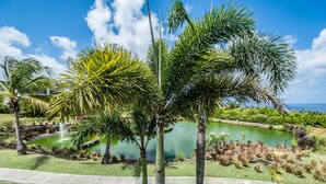 Un jardín ajardinado con un estanque, palmeras y un cielo azul despejado.