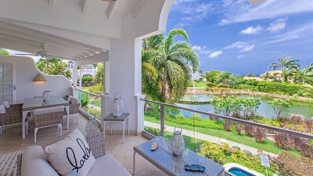 Un balcón con vistas a un jardín ajardinado, una piscina y un cielo despejado.