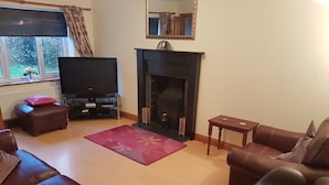 A living room with a fireplace, leather sofas, a television, and a window with curtains. - Spacious House, Just Five Minutes Walk From Beach, Perfect for Families/Surfers (Bude)