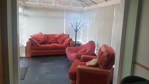 A room with a red sofa set, a small table, and a decorative tree. - Spacious House, Just Five Minutes Walk From Beach, Perfect for Families/Surfers (Bude)