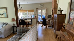 A spacious living room with a sofa, a dining area with chairs, a kitchen in the background, and a large window with curtains. - Large open plan cottage in conservation village just outside York. 3 night deals (York)