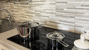 A modern kitchen with a black induction cooktop, stainless steel pots, a coffee maker, and a spice rack on the wall.