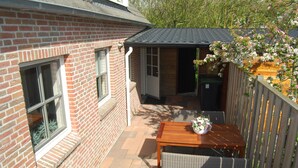 A brick house with a small patio area, a wooden table, wicker chairs, and a flower pot. - Detached holiday home in Westkapelle for 4 people. (Westkapelle)