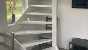 A spiral staircase with white railings in a room with a TV mounted on the wall and a window with a view of buildings outside. - Detached holiday home in Westkapelle for 4 people. (Westkapelle)