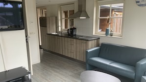 A modern kitchen with a built-in oven, a coffee maker, and a window with a view. There is a blue leather sofa and a small white table in the living area. - Detached holiday home in Westkapelle for 4 people. (Westkapelle)