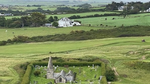 Un cementerio con una iglesia de piedra, rodeado de campos verdes y algunas casas al fondo.
