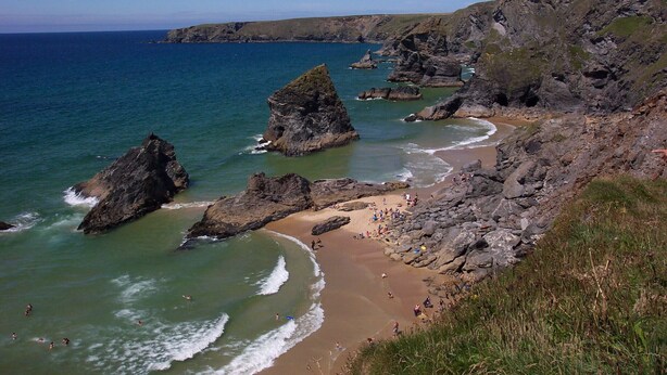 Paisaje costero con afloramientos rocosos, una playa de arena y el mar.