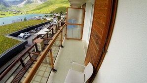 Un balcon avec vue sur un lac, des montagnes et des voitures garées.