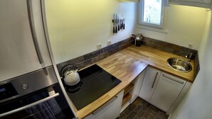 Une cuisine moderne équipée d’un four encastré, d’une plaque de cuisson, d’un évier et d’une fenêtre laissant entrer la lumière naturelle.