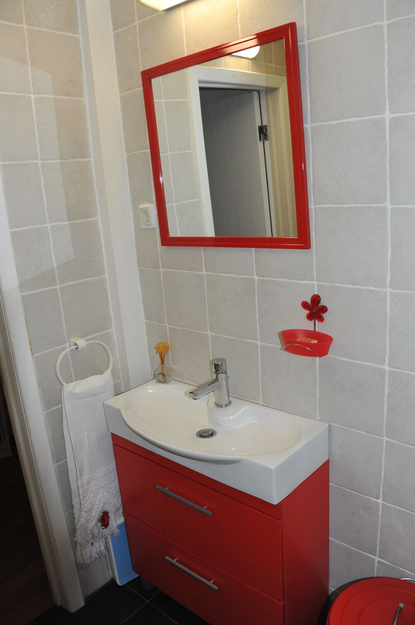 A bathroom with a white sink, red cabinet, and a red-framed mirror.