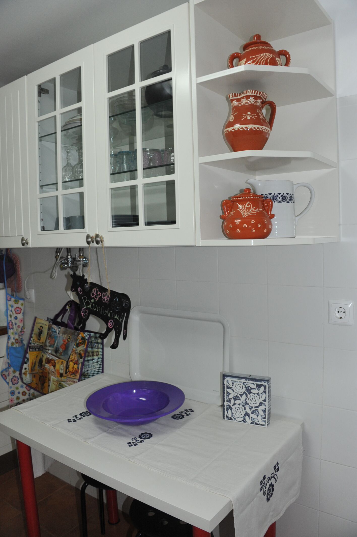 A kitchen with white cabinets, a purple bowl on the counter, and a white tablecloth.