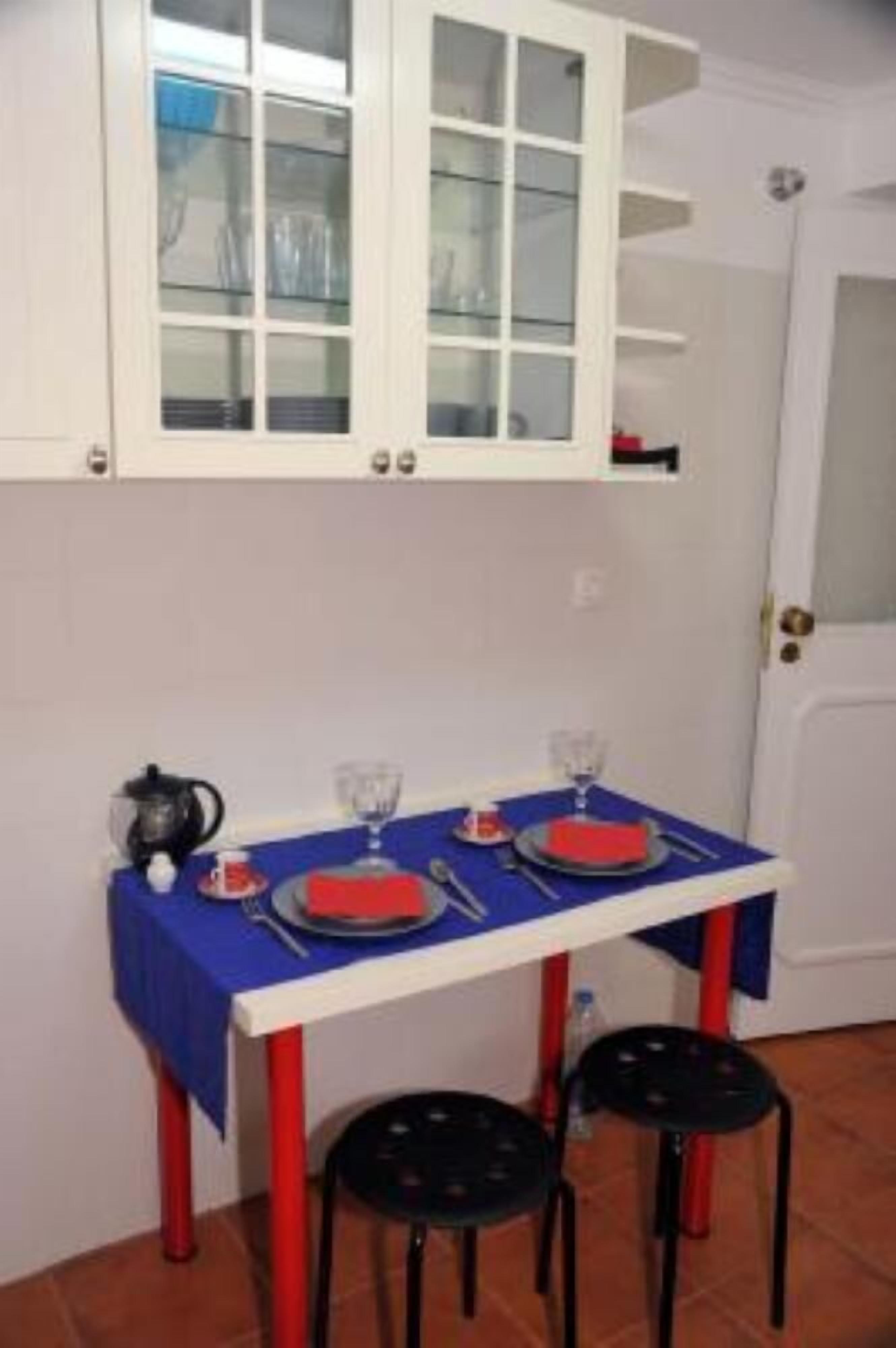 A small dining area with a table set for two, a white cabinet above, and red stools.