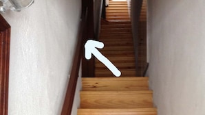 Een houten trap met aan één kant een witte muur en aan de andere kant een houten deur.
