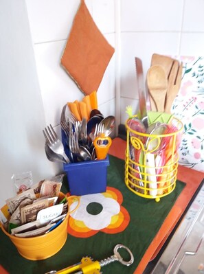 A kitchen counter with utensils, a yellow container with sugar packets, and a decorative mat.