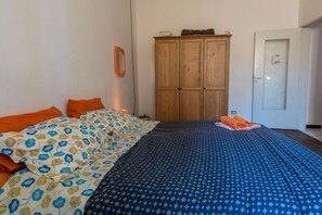 A bedroom with a bed, orange pillows, a wooden wardrobe, and a door.