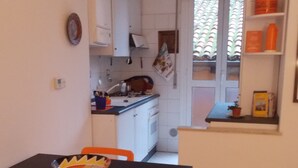 Cuina compacta amb armaris blancs, taula de dinar petita amb caires taronja i finestra que mostra un teulat amb rajoles.
