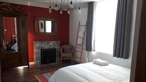 Un dormitorio con cama, chimenea, una silla, una escalera y una ventana con cortinas.