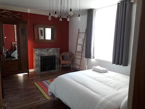 Une chambre à coucher avec un lit, une cheminée, une chaise, une échelle et une fenêtre avec des rideaux.