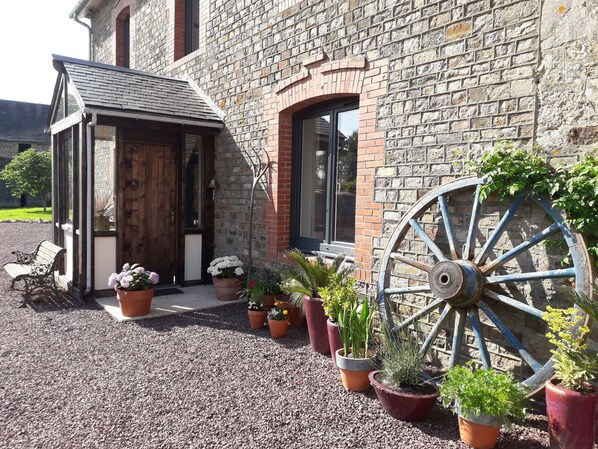 A rustic stone building with a wooden door, a small porch with a bench, and potted plants.