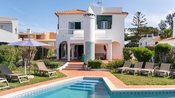 Una villa de dos plantas con piscina, mobiliario de exterior y jardín.