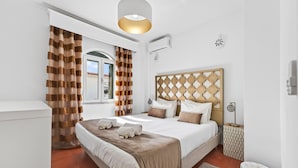 Habitación de hotel con una cama grande, una mesita de noche, una ventana con cortinas, un aire acondicionado de pared y un panel decorativo.